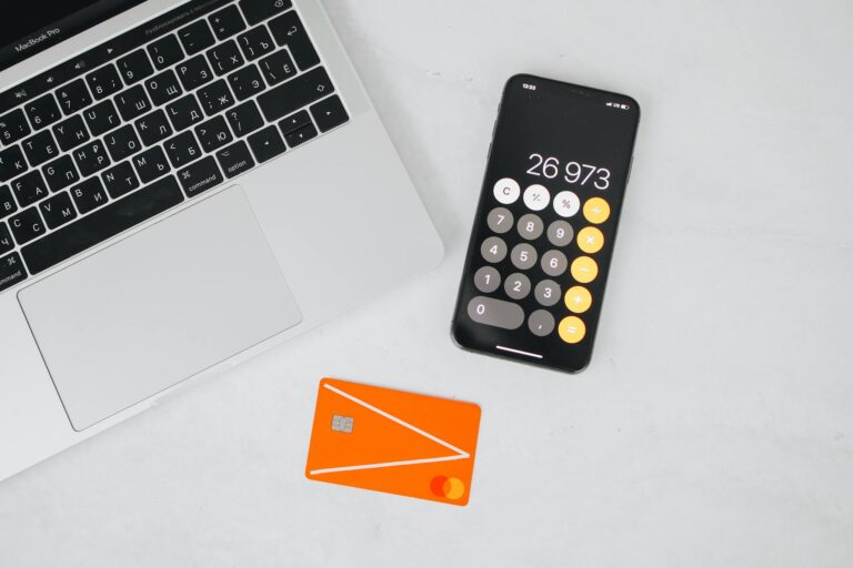A laptop, smartphone displaying calculator, and credit card on a white table.